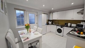 Una cocina moderna con armarios blancos, una mesa de comedor para cuatro personas y una lavadora.