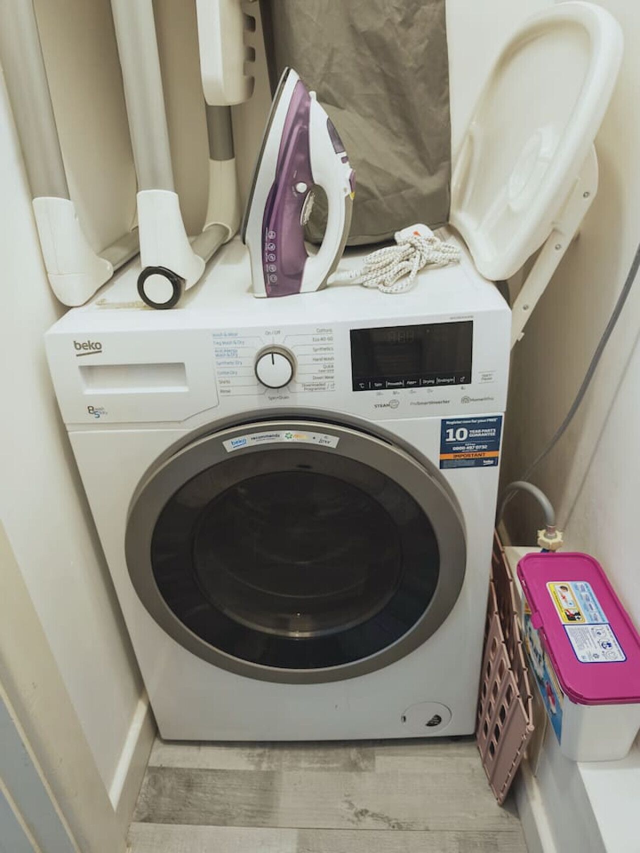 A compact, white front-loading washing machine with a digital display, a control panel, and a 10-year warranty sticker.