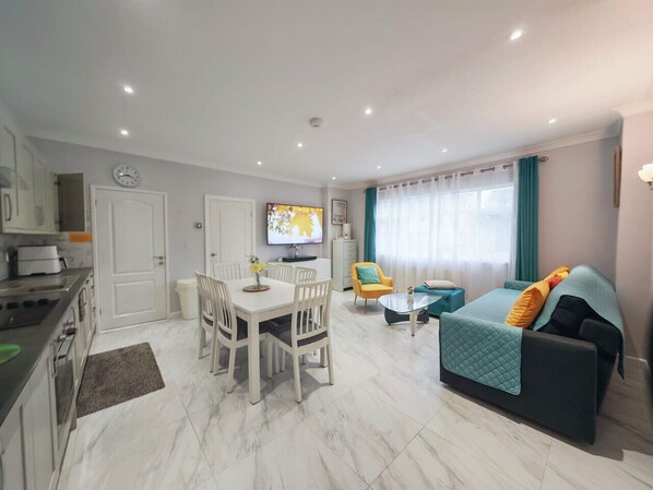 A modern apartment with a dining area, a living room with a sofa and TV, and a kitchen.