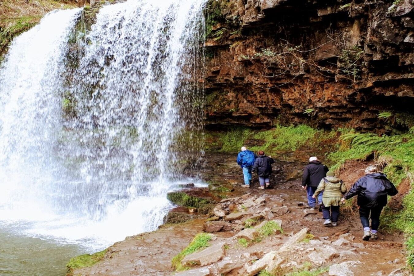 A waterfall with hikers on a rocky path.