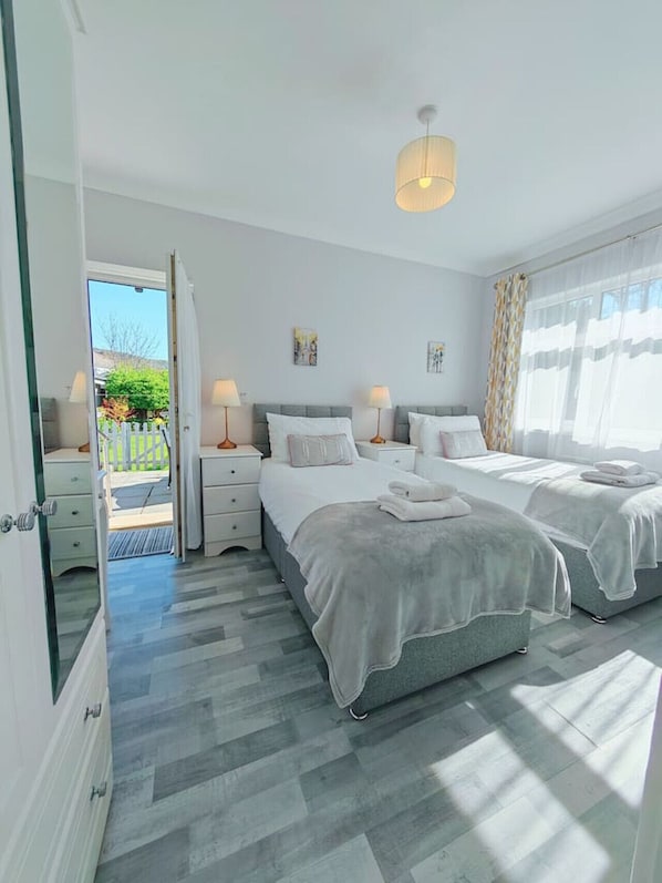 A modern bedroom with two beds, a large window with sheer curtains, and a view of the outdoors.