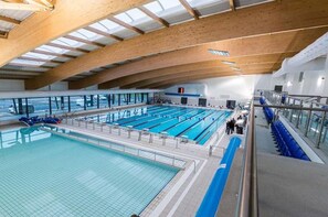 An indoor swimming pool with multiple lanes, a wooden ceiling, and a glass barrier.