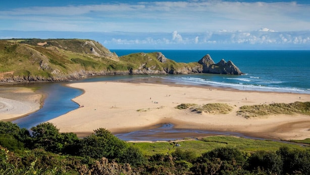 Eine Küstenlandschaft mit Sandstrand, einer geschwungenen Bucht und Felsformationen.