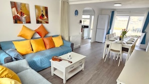 Ein Wohnzimmer mit einem blauen Sofa, einem Couchtisch und einem Essbereich mit Tisch für vier Personen.