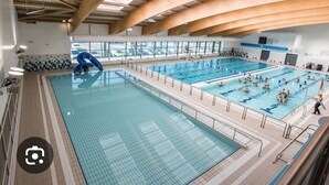 Ein Hallenbad mit mehreren Bahnen, einer Rutsche und einem Rettungsschwimmerstand.
