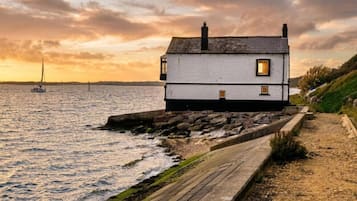 Ett hus vid kusten med en gångstig av sten som leder till entrén, beläget vid havet med en segelbåt i bakgrunden.