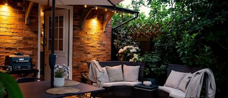 An outdoor patio with a brick wall, a grill, wicker furniture, and a dining table.