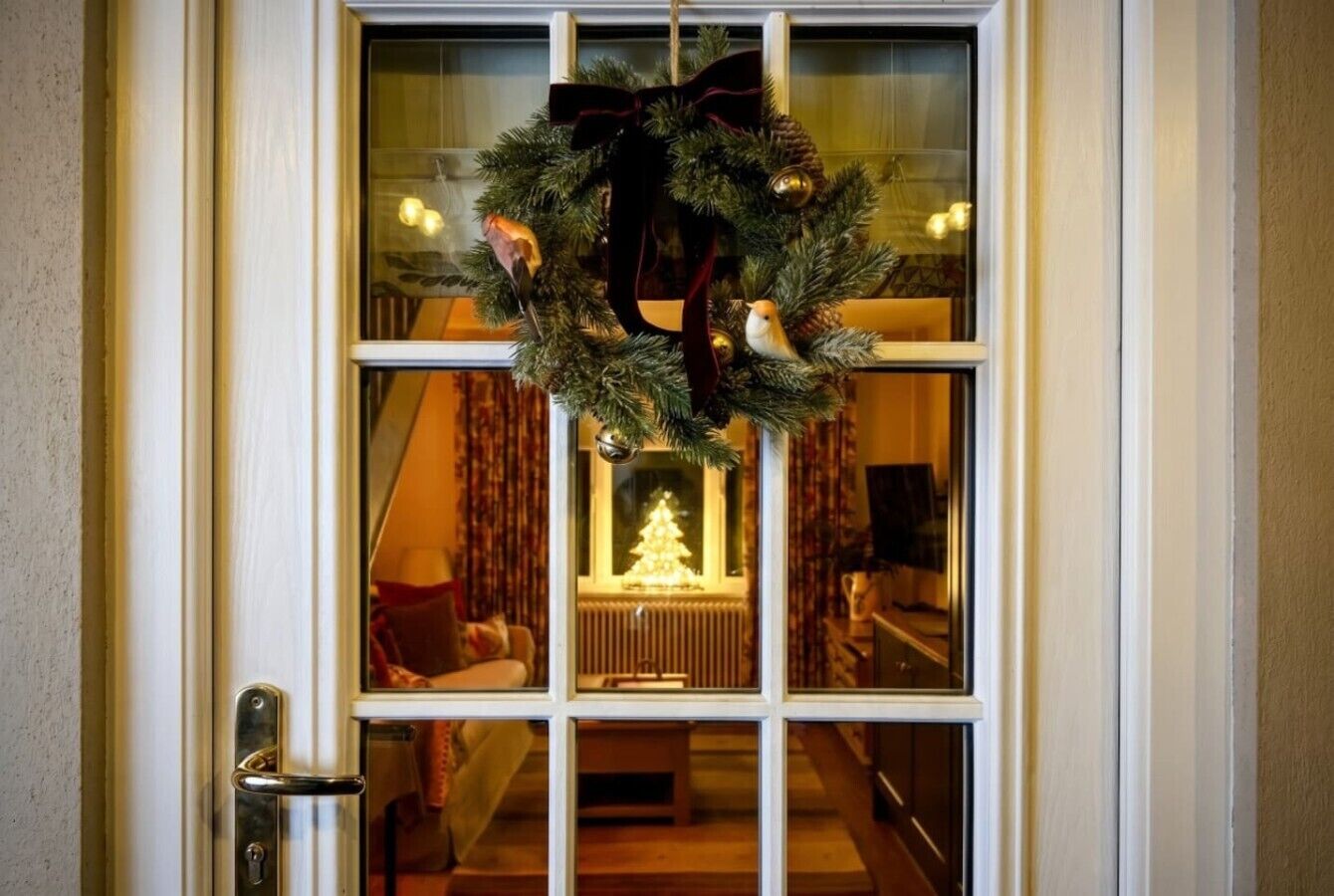 A door with a wreath, a Christmas tree inside, and a view of a living room with a sofa and a table.