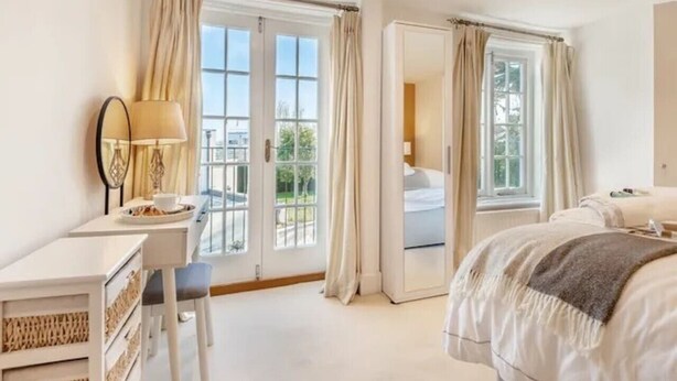 Une chambre d’hôtel avec un lit, un bureau doté d’une lampe et une vue sur l’extérieur grâce à de grandes fenêtres.