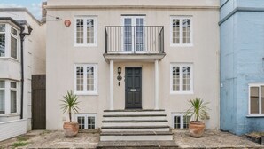 Un bâtiment à deux étages avec une porte d’entrée noire, des fenêtres à cadre blanc et un balcon.