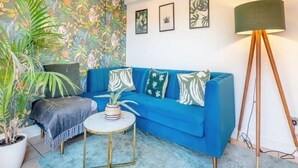 Un salon avec un canapé bleu, une table basse ronde, un lampadaire et une grande plante en pot.