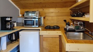 A compact kitchen with wooden walls and ceiling, equipped with a coffee maker, two microwaves, a toaster oven, a small refrigerator, and a sink. - Cozy, Quite, Private Loft, Near Ocean, 
Center of Haida Gwaii (Port Clements) (Port Clements)