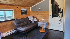 A cozy room with a wooden ceiling, a brown leather sofa, a small table with a vase, and a door with a black device mounted on it. - Cozy, Quite, Private Loft, Near Ocean, 
Center of Haida Gwaii (Port Clements) (Port Clements)