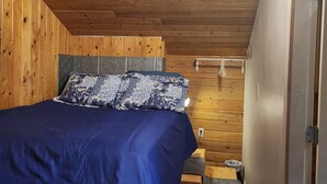 A bedroom with a wooden ceiling, a bed with a blue bedspread, and a patterned pillow. - Cozy, Quite, Private Loft, Near Ocean, 
Center of Haida Gwaii (Port Clements) (Port Clements)