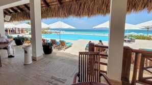 A beachside view with a pool, lounge chairs, umbrellas, and a thatched roof structure. - Cana Rock Star Condo Hotel (Punta Cana)