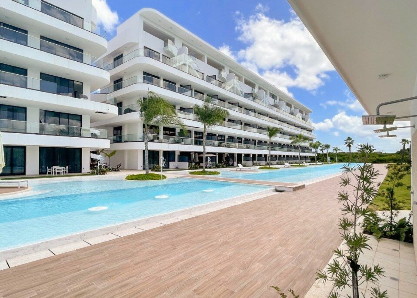 A modern hotel with multiple balconies, a large swimming pool, and a well-maintained garden area.