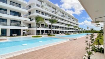 A modern hotel with multiple balconies, a large swimming pool, and a well-maintained garden area.