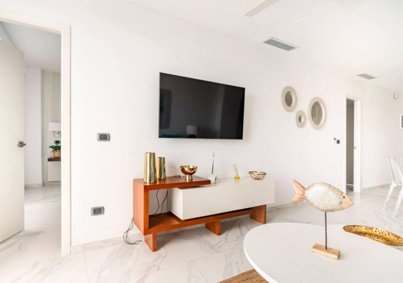 Ein modernes Wohnzimmer mit einem weißen Sofa, einem an der Wand befestigten Flachbildfernseher und einem runden Couchtisch.