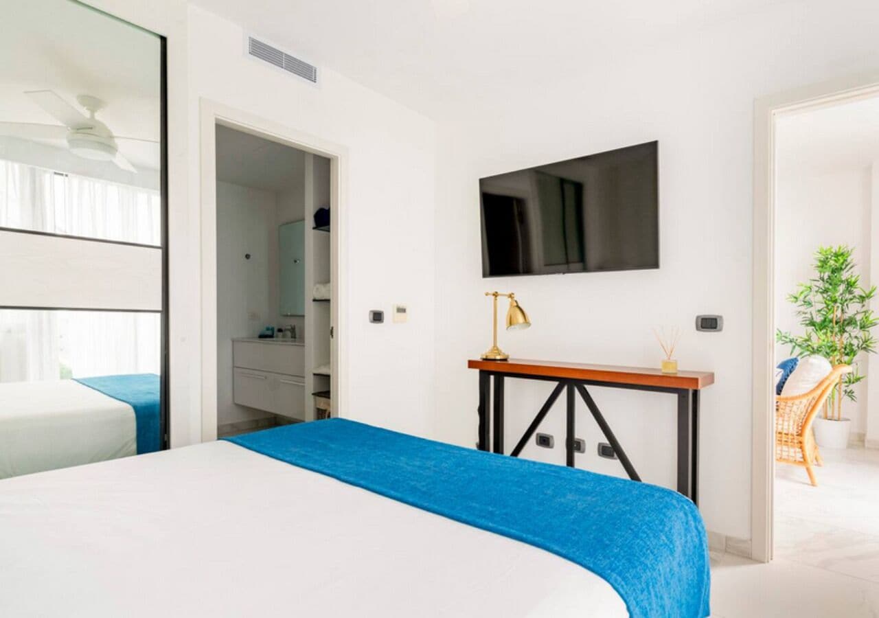 Une chambre d’hôtel moderne avec un grand lit, un téléviseur fixé au mur, un bureau avec une lampe et une vue sur la salle de bain.