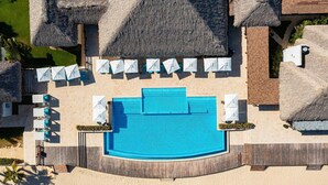 An aerial view of a resort with a central swimming pool, thatched-roof structures, and sun loungers. - Cana Rock Star Condo Hotel (Punta Cana)