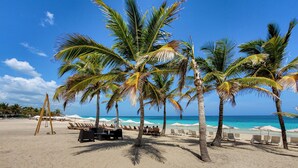 A beach with palm trees, lounge chairs, and umbrellas. - Cana Rock Star Condo Hotel (Punta Cana)