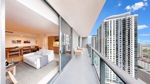 A modern hotel room with a balcony, a dining area, and a view of high-rise buildings.