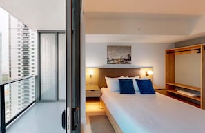 Habitación de hotel moderna con una cama grande, una mesita de noche, un estante en la pared y vistas a la ciudad desde la ventana.
