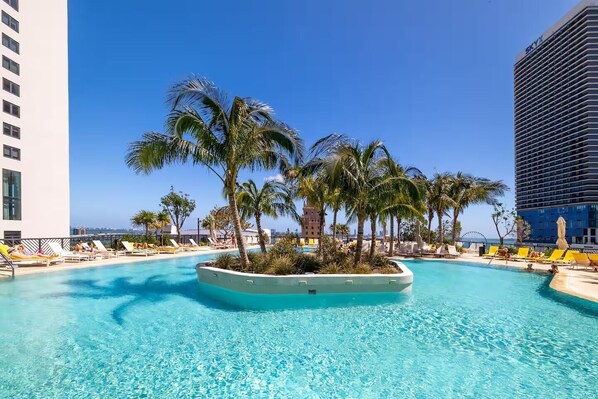 A pool area with palm trees, lounge chairs, and a view of the ocean.