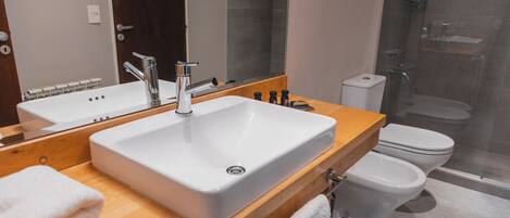 Un baño moderno con un lavabo grande blanco, un tocador de madera, un espejo, un inodoro y una cabina de ducha de vidrio.