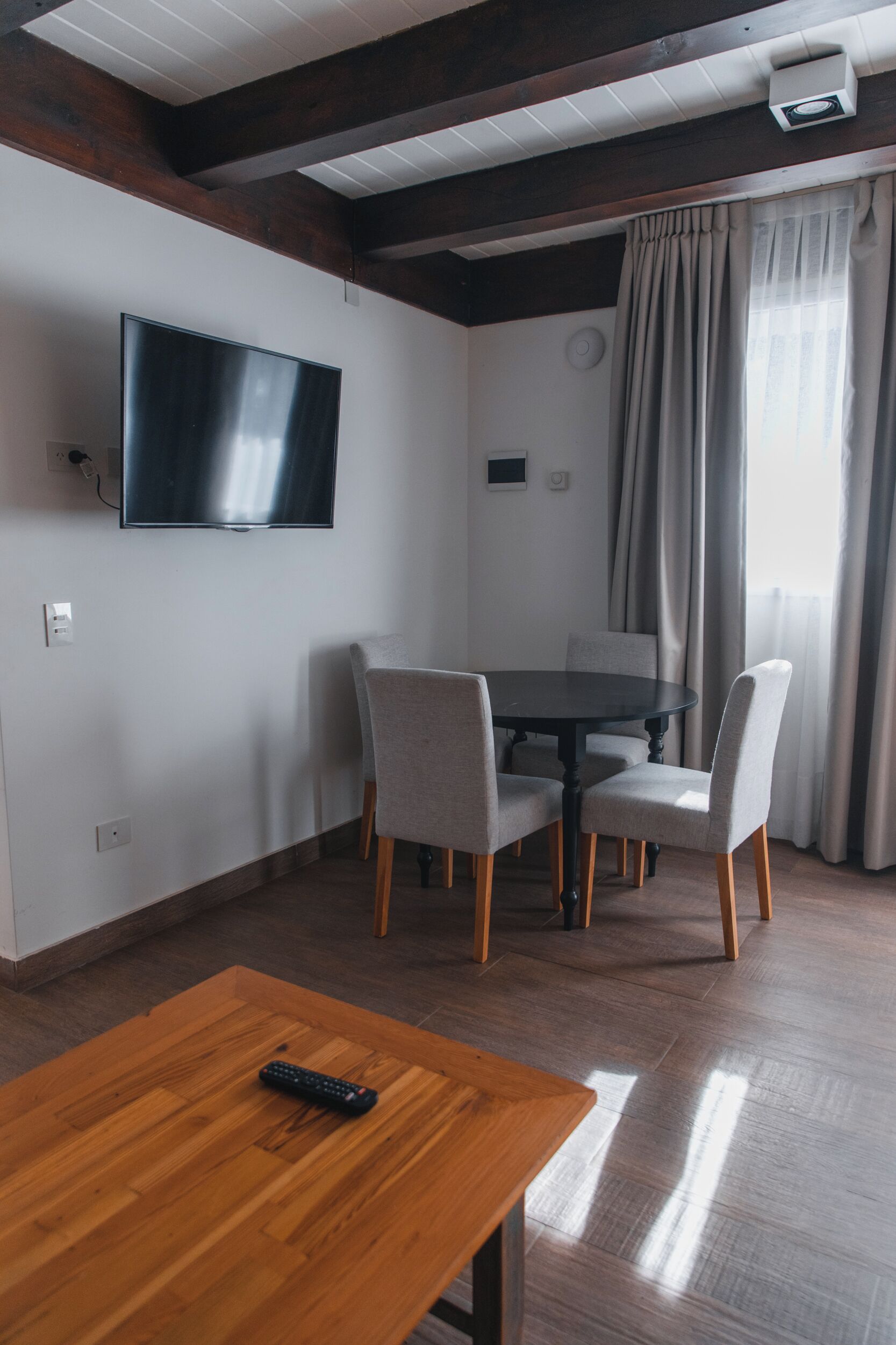 Una sala de estar moderna con una mesa de comedor de madera, sillas tapizadas en gris, un televisor de pantalla plana montado en la pared y un ventilador de techo.