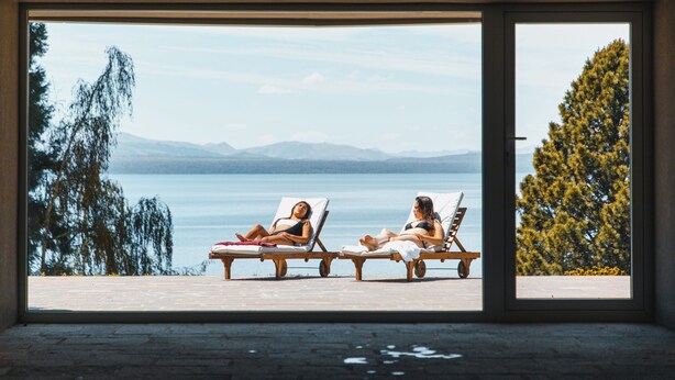 Deux fauteuils confortables sont placés face à un lac, avec des montagnes en arrière-plan.