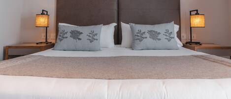 A neatly made bed with a brown headboard, two bedside lamps, and decorative pillows with floral designs.