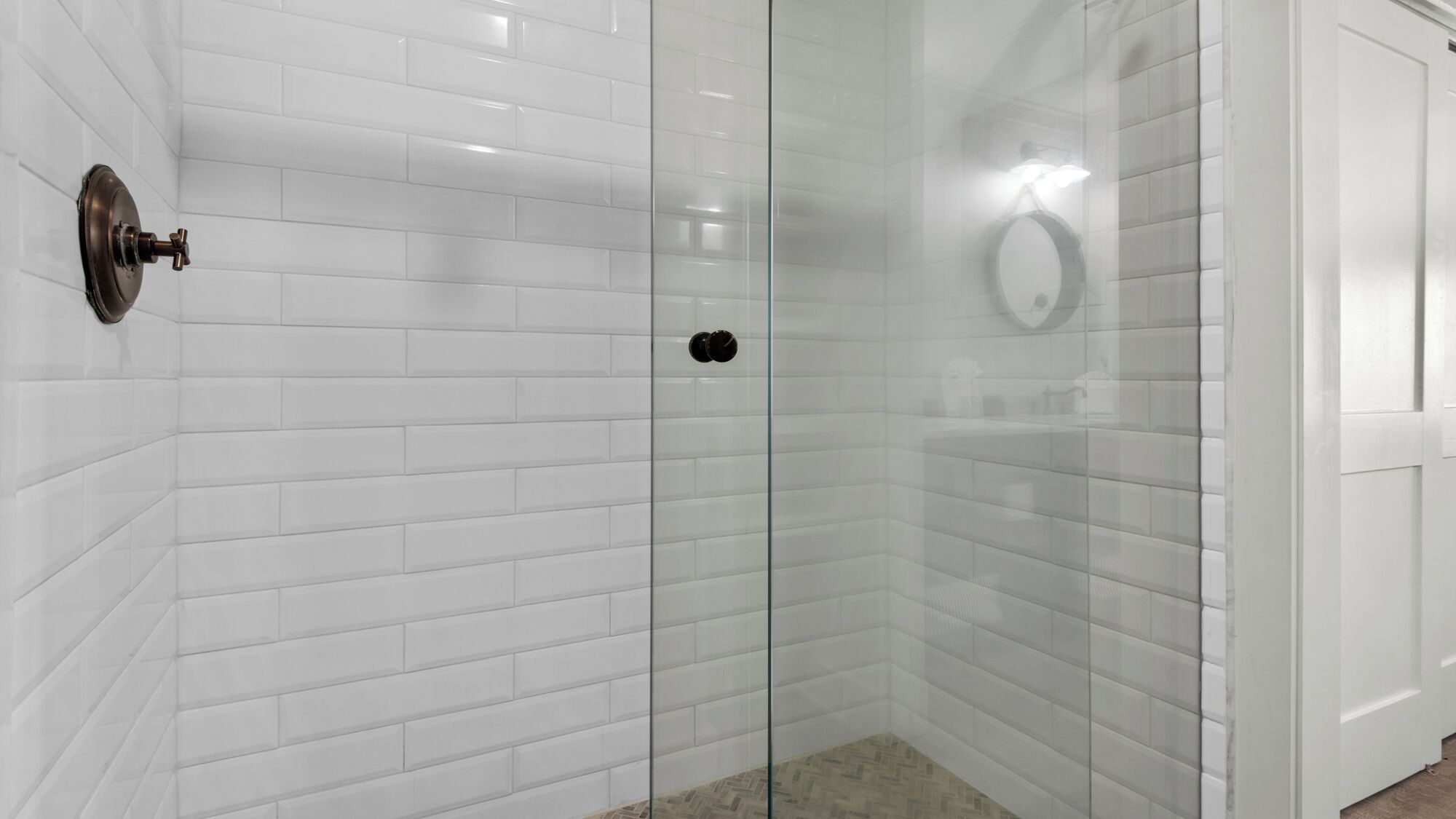 Casa de banho moderna com azulejos brancos, cabine de duche em vidro e sanita visível.