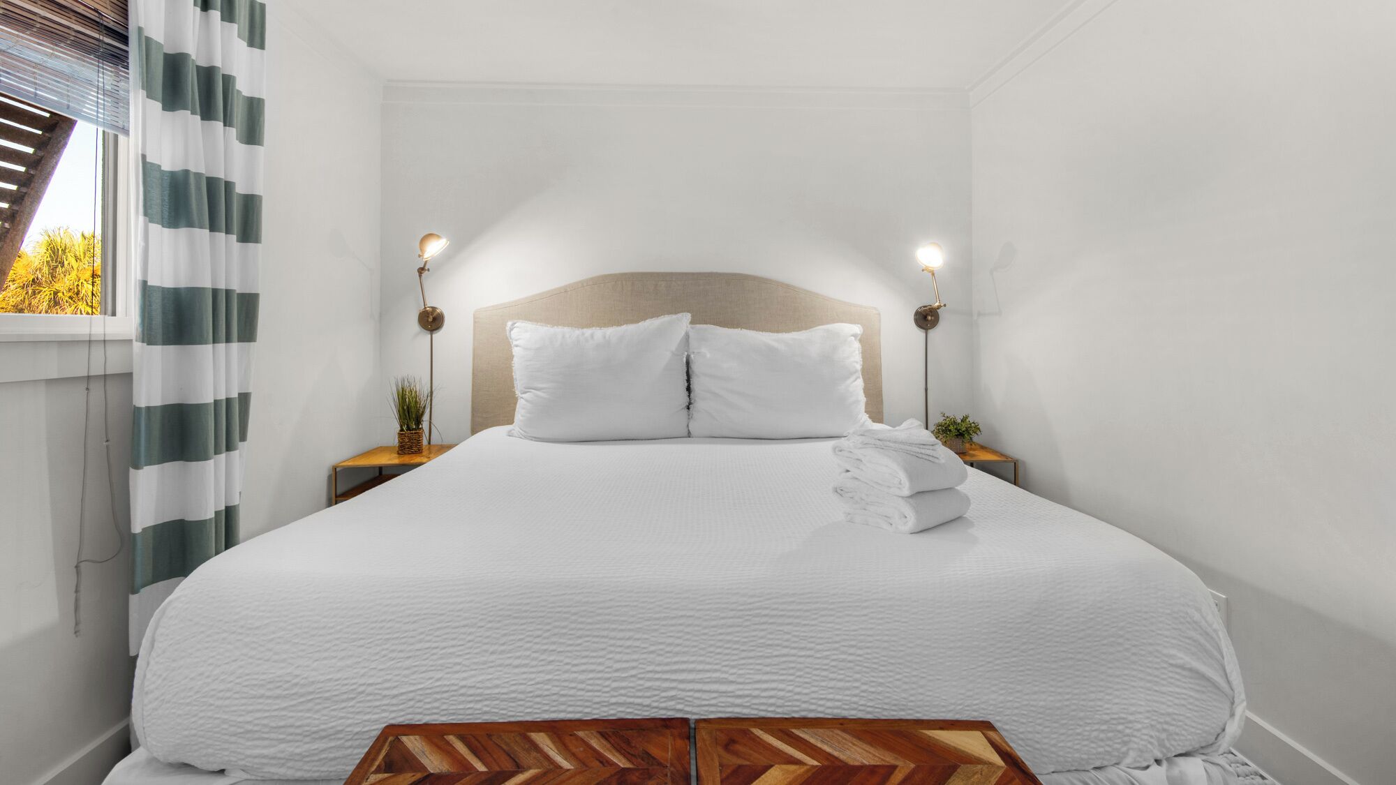 A neatly made bed with white bedding, two bedside lamps, and a wooden headboard.