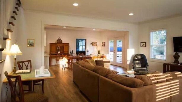 A spacious living room with a sofa, dining table, and chairs. There is a kitchen area in the background with a dining table and chairs.