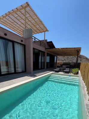 Un área de piscina moderna con agua cristalina, una pérgola de madera y mobiliario de exterior.