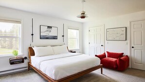 Un dormitorio con cama de madera, ropa de cama blanca, una silla roja y obras de arte en las paredes.