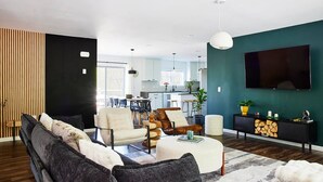 Ein modernes Wohnzimmer mit einer Couch, Sesseln, einem Couchtisch und einem Fernseher.