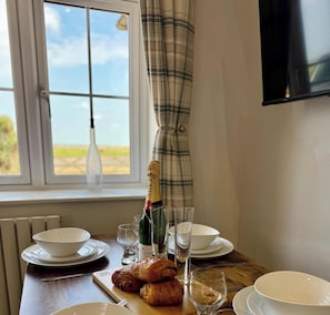 A dining table with plates, glasses, a bottle of champagne, and croissants.