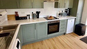 A modern kitchen with green cabinets, a stainless steel range hood, a built-in oven, and a microwave. - Four Counties Cottages, Collyweston (Collyweston)