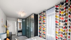 Une chambre à coucher moderne, avec un lit, une table de chevet, un miroir, une armoire et une porte donnant sur une autre pièce.