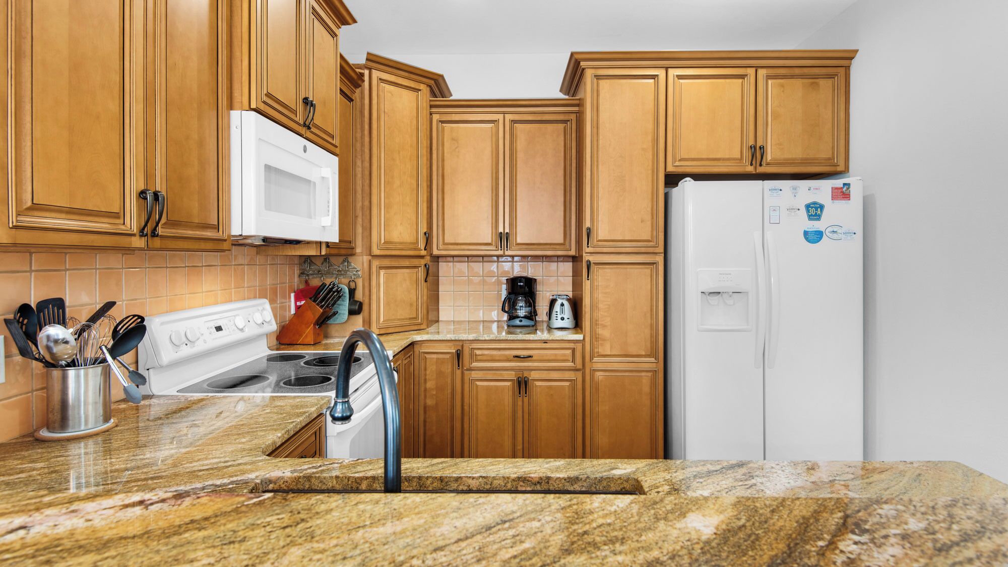 A kitchen with wooden cabinets, a white stove, a microwave, a coffee maker, and a refrigerator.