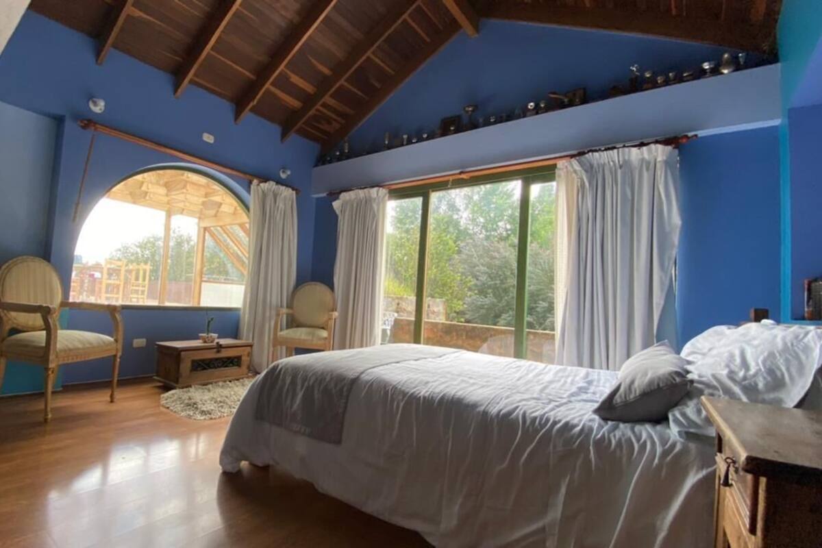 A bedroom with a bed, two chairs, a small table, and a large window with curtains.