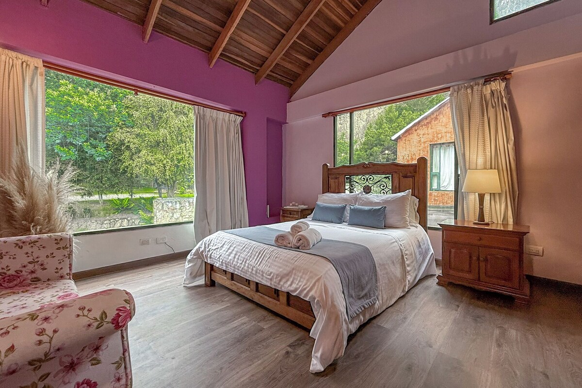 A bedroom with a wooden bed, large windows, and a view of greenery outside.