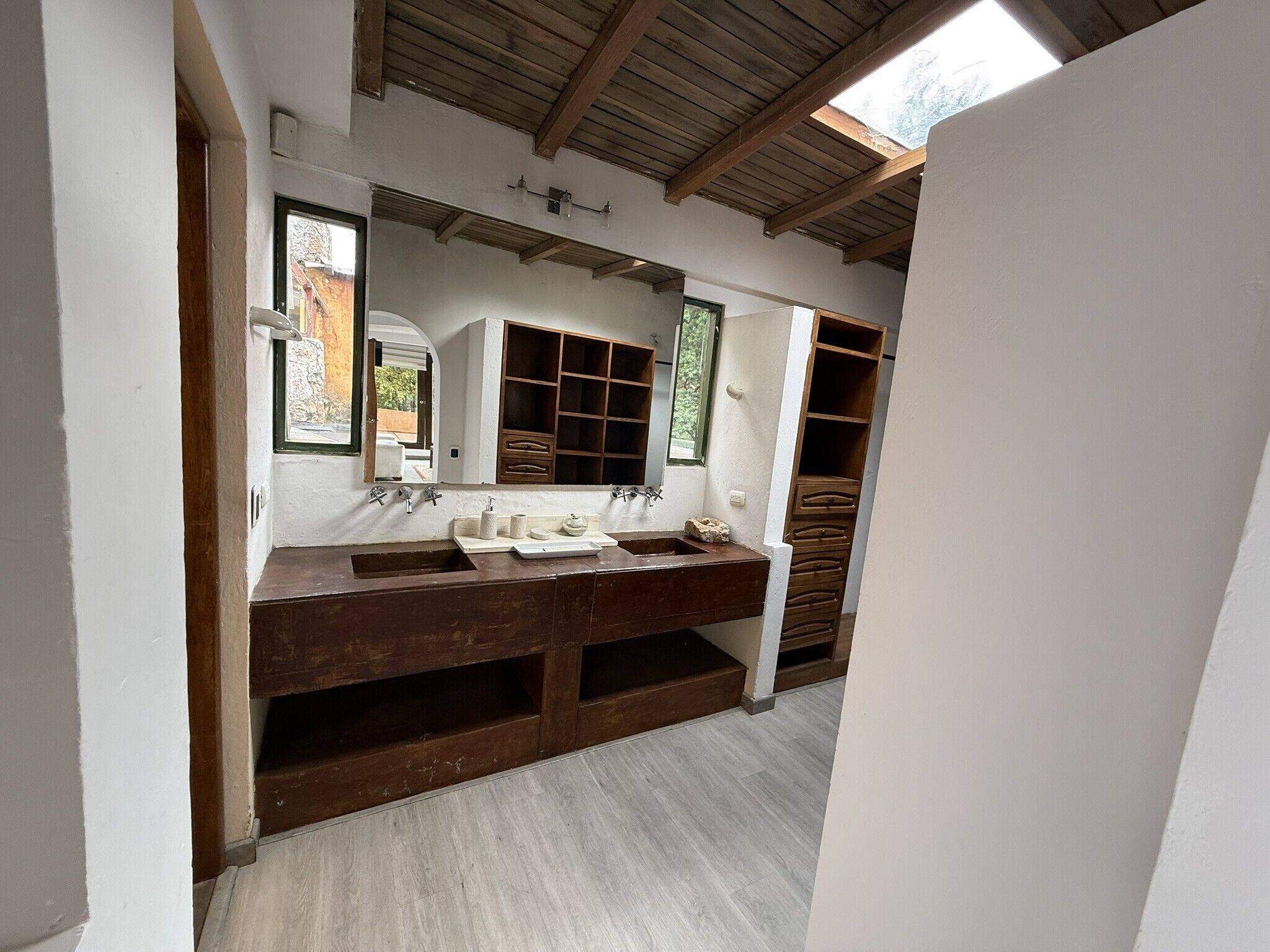 Un baño con tocador de madera, un espejo grande y un tragaluz.