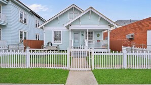 A row of two-story houses with a white picket fence, a front porch, and a small front yard.