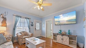 A living room with a ceiling fan, a television, a couch, a coffee table, and a wooden floor.