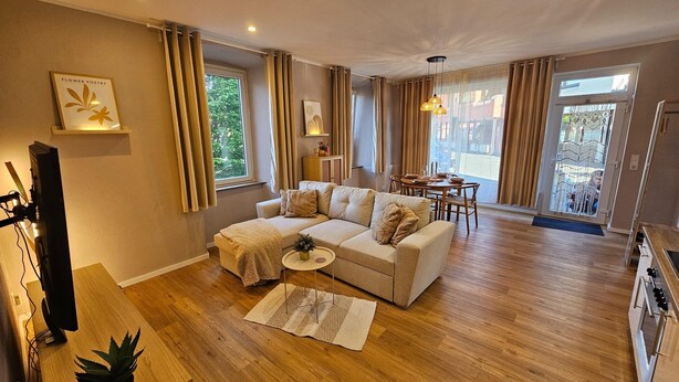 A modern living room with a sofa, a dining table, and a kitchen area.