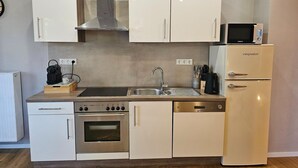 A compact kitchen with white cabinets, a stainless steel range, a built-in oven, a microwave, and a refrigerator.
