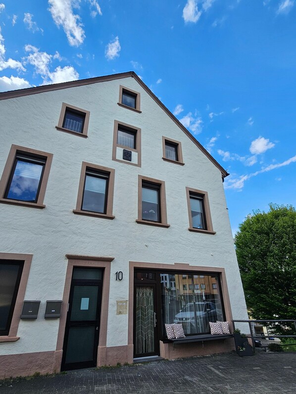 Un edificio de varios pisos con fachada blanca y marcos de ventana marrones. El edificio tiene techo plano y una puerta de vidrio grande con diseño decorativo.